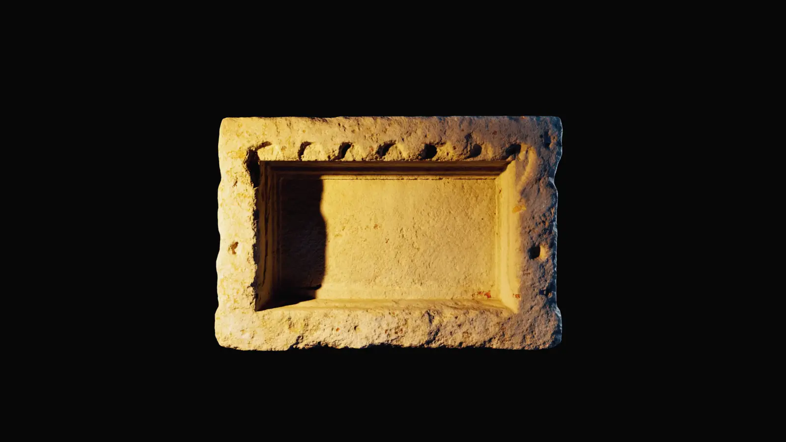 An empty carved stone niche in a black wall, one shaft of gold light falling into it